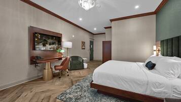 A hotel room with a large bed, a desk, a chair, a television, and a chandelier.