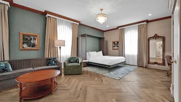 Quarto de hotel com cama, sofá, poltrona e mesa de centro de madeira.