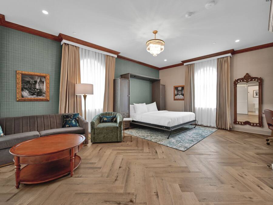 Una habitación de hotel con cama, sofá, sillón y una mesita de centro de madera.