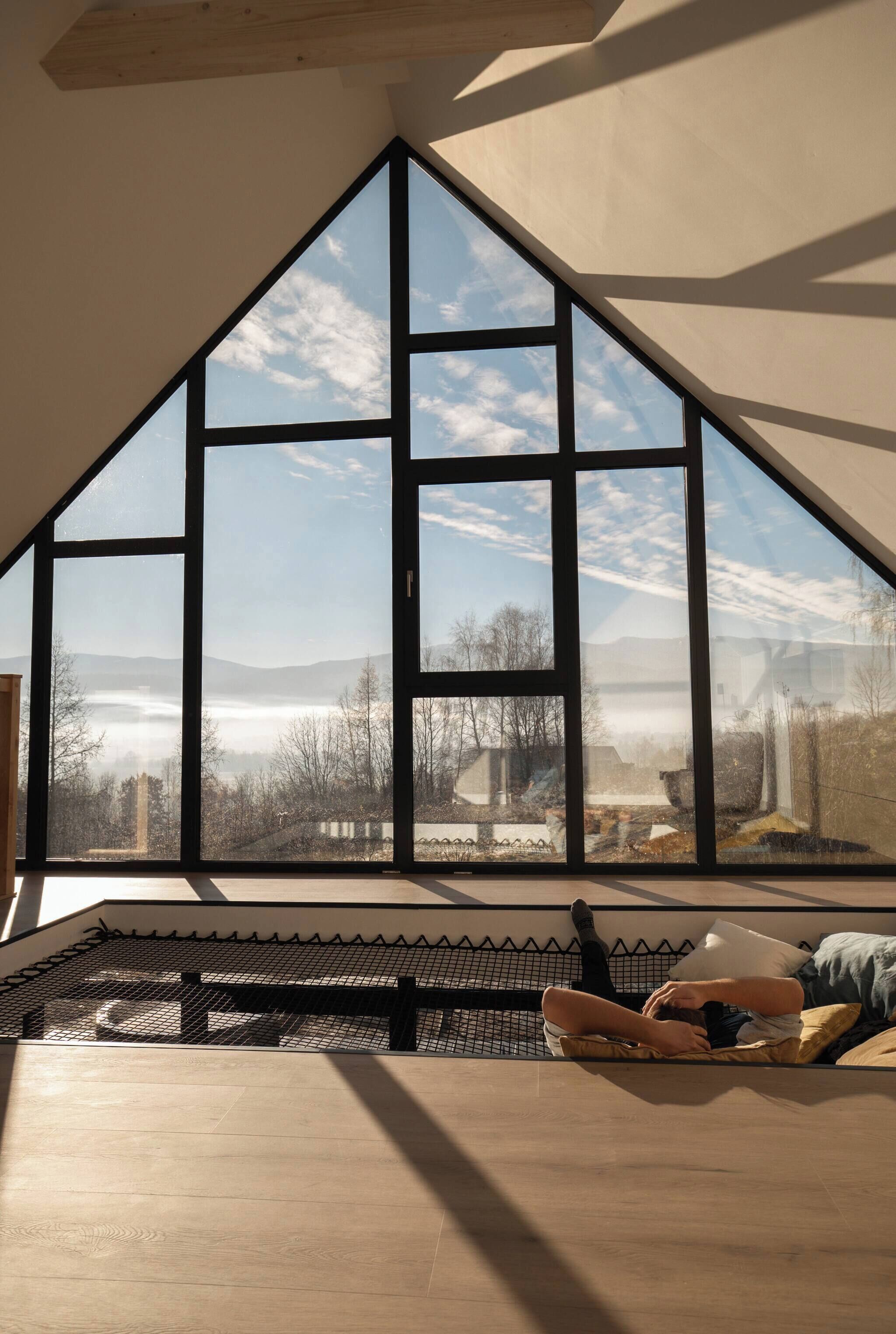A room with a large triangular window, a wooden ceiling, and a view of a landscape with trees and mountains.