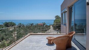 Ein Balkon mit Meerblick, ein Korbstuhl und eine Glastür.