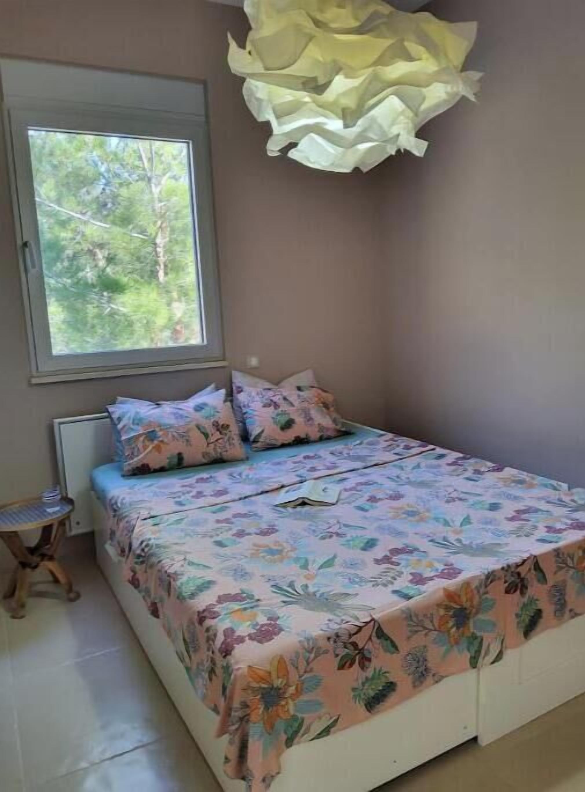 A bedroom with a bed, a window, a bedside table, and a hanging light fixture.