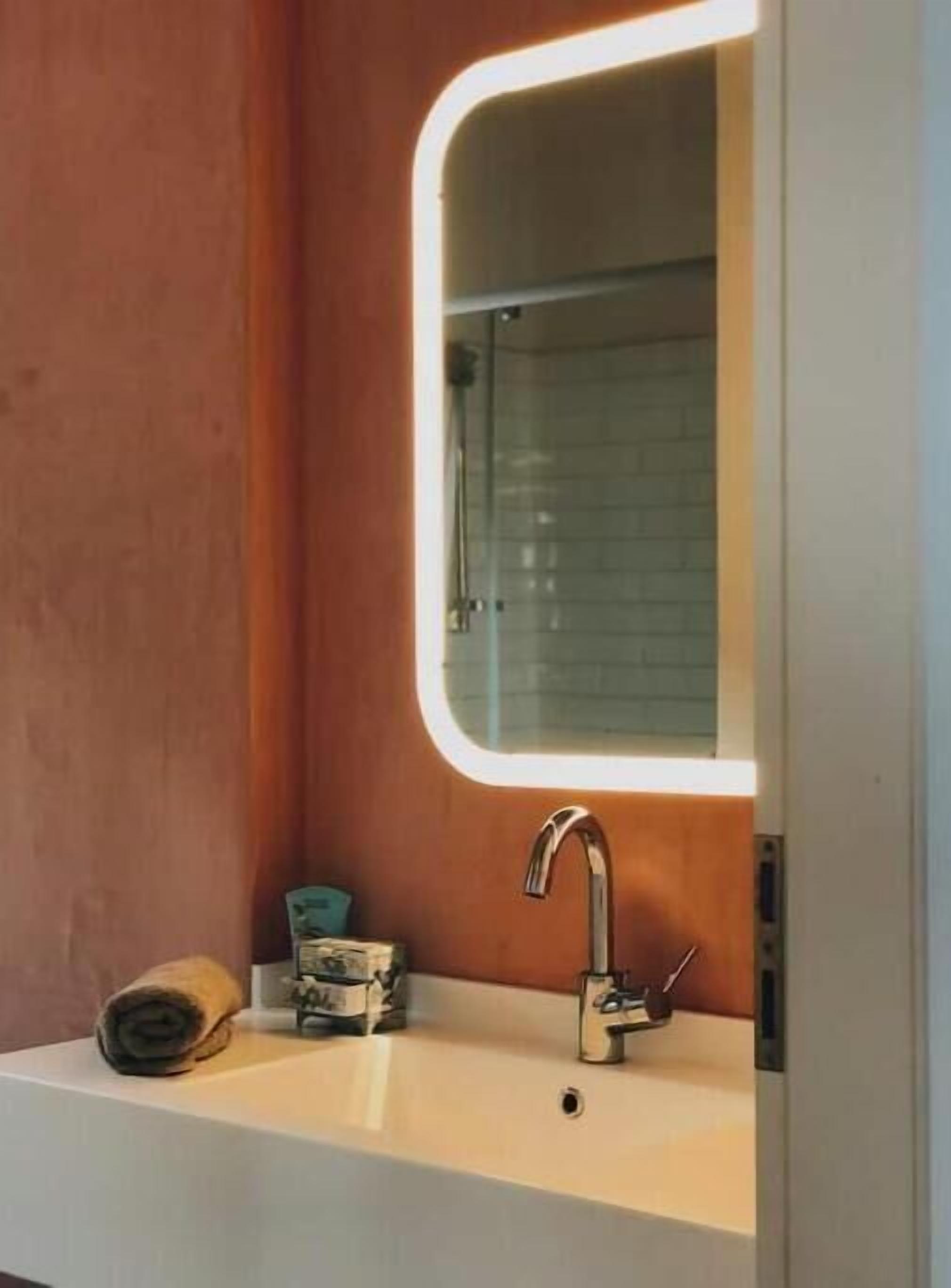 Un baño con un lavamanos blanco, un espejo con luz y una toalla en la encimera.