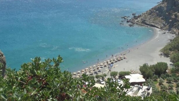 Blick auf die Küste mit Strand, felsigen Klippen und einem klaren, blauen Meer.