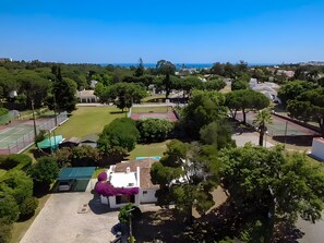 An aerial view of a residential area with houses, a tennis court, and a clear view of the sea. - Casa Charlotte – 4 Bedroom Villa with Private Pool near Albufeira Beaches (Olhos de Água)