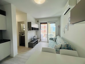 A modern apartment with a kitchenette, a sofa, a dining table, and a balcony with a view. - Bright Apartment 150m From the Beach (San Michele al Tagliamento)