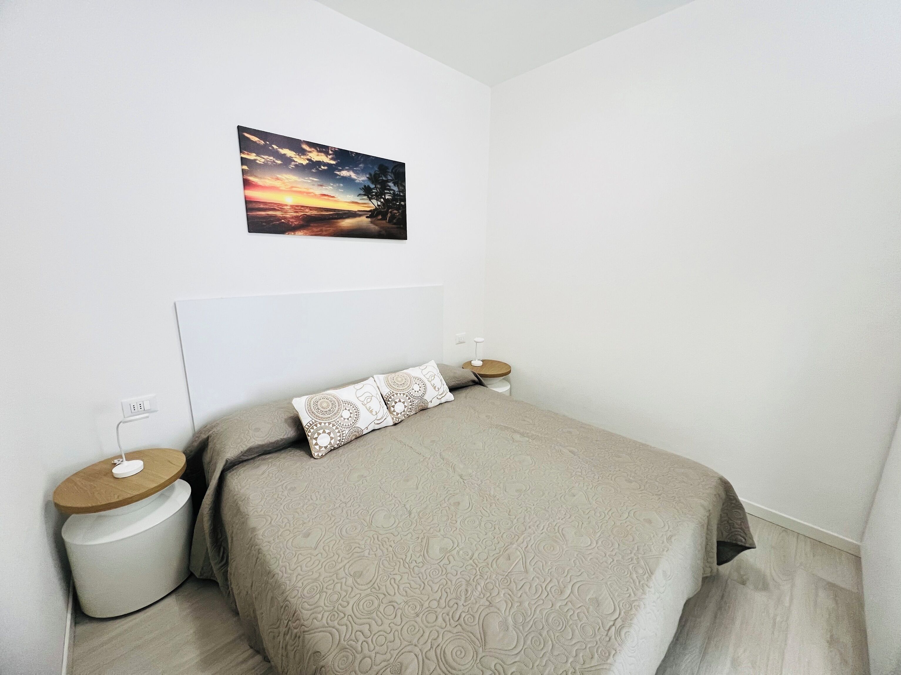 Une chambre à coucher comprenant un lit, deux tables de chevet, une commode, un tableau accroché au mur et une prise de courant.