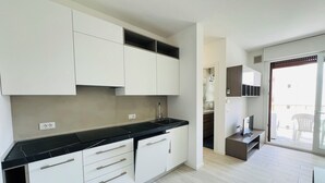 A modern kitchen with white cabinets, black countertops, and a wooden floor. - Bright Apartment 150m From the Beach (San Michele al Tagliamento)