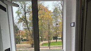 A room with a sliding glass door leading to a balcony with a view of a park and trees. - Spacious, light-filled apartment inside the ancient town walls, with great views (Treviso)