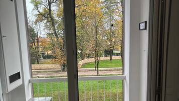 A room with a sliding glass door leading to a balcony with a view of a park and trees.