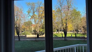 A view through a window with a white railing, trees with autumn foliage, and a building in the background. - Spacious, light-filled apartment inside the ancient town walls, with great views (Treviso)