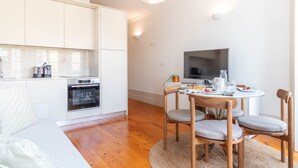 Una cocina moderna con armarios blancos, horno integrado y zona de comedor con mesa redonda y cuatro sillas.