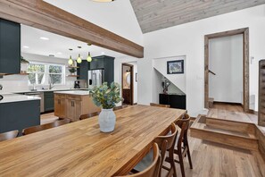 A modern kitchen with a wooden dining table, a vase of flowers, and a staircase leading to another level. - Cabin w/ hot tub near Cana Island Lighthouse (Baileys Harbor)