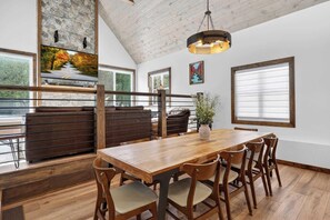 A dining area with a wooden table and chairs, a hanging light fixture, and a stone wall with a painting. - Cabin w/ hot tub near Cana Island Lighthouse (Baileys Harbor)