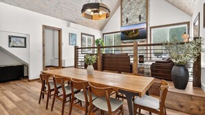 A dining area with a wooden table and chairs, a stone wall, and a large window with a view. - Cabin w/ hot tub near Cana Island Lighthouse (Baileys Harbor)