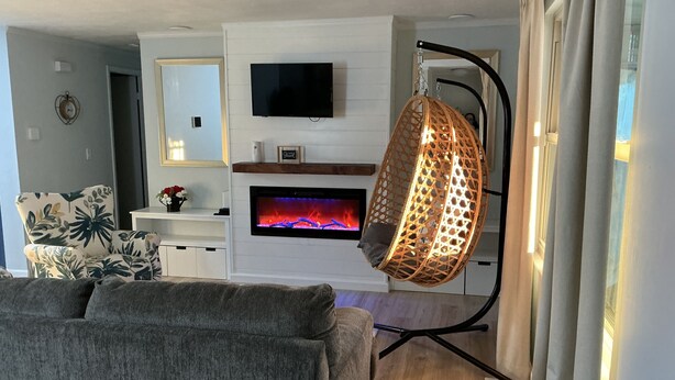 Een woonkamer met een bank, een televisie, een open haard en een hangstoel.