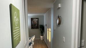 Een gang met een groen bord, een ingelijst kunstwerk, een plant en een wandlamp.