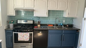Een keuken met witte kasten, een roestvrijstalen fornuis, een vaatwasser en een gootsteen met een kraan.