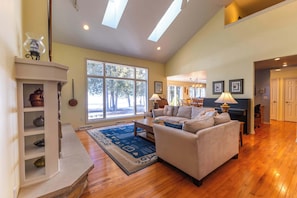 A spacious living room with a fireplace, a sofa, a coffee table, and a large window. - Quiet Door County Retreat w/ Private Bay Access (Sturgeon Bay)