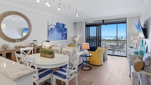 Een moderne woonkamer met een eetgedeelte, een grote ronde spiegel, een blauw abstract schilderij, en een balkon met uitzicht.
