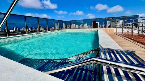 A rooftop pool with a city skyline view, glass railings, and a wooden deck. - Compact Time - Miramar Hospedagens  (João Pessoa)