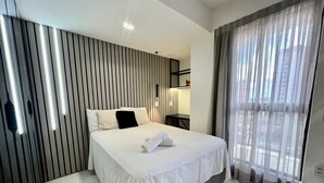 A modern hotel room with a bed, a bedside table, a lamp, a window with curtains, and a wall with vertical lines. - Compact Time - Miramar Hospedagens  (João Pessoa)