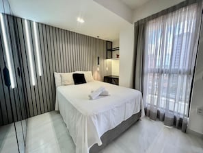 A modern hotel room with a bed, a bedside table, a lamp, a window with curtains, and a wall with vertical lines.