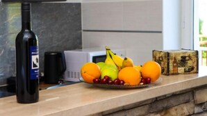 A kitchen counter with a bottle of wine, a microwave, a fruit bowl with oranges and bananas, and a decorative box. - Delux Konavle Village Apartment (Konavle)