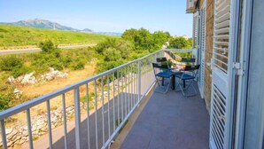A balcony with a view of a green landscape and mountains, a table with chairs, and a building with a white railing. - Delux Konavle Village Apartment (Konavle)