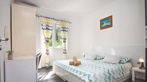 A bedroom with a bed, a nightstand, a desk, a chair, a window with curtains, and a framed picture on the wall. - Delux Konavle Village Apartment (Konavle)