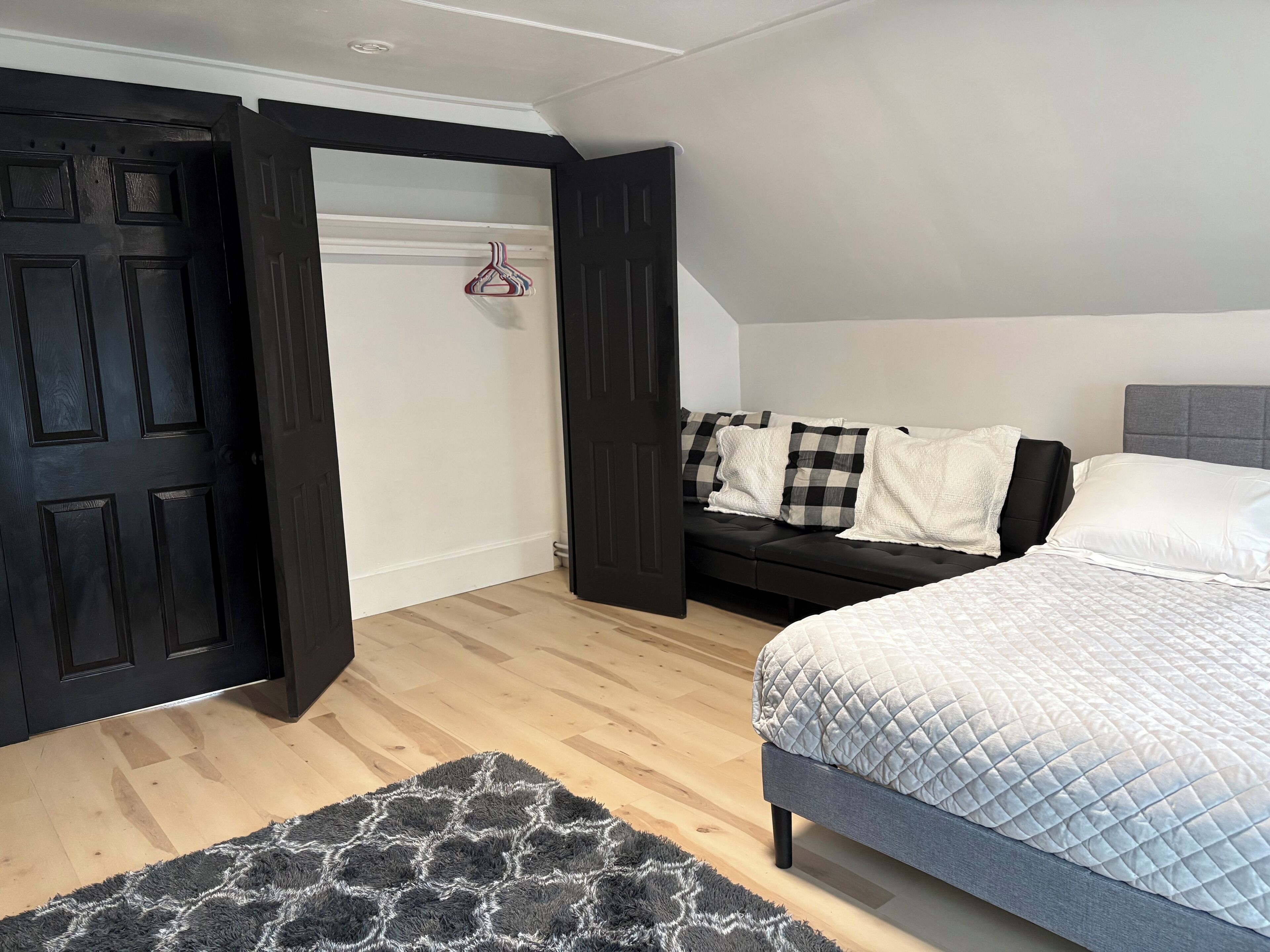 A bedroom with a bed, a sofa, a black door, and a wooden floor.