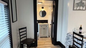 A hallway leading to a dining area with a table set for two, a chair, a radiator, and a mirror on the wall.