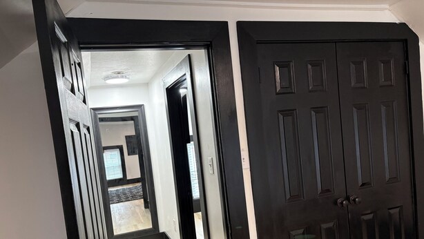 A hallway with a wooden floor, a black door, and a white wall.