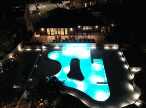 Una piscina exterior de forma singular, envoltada per una zona de solàrium ben il·luminada amb seients.
