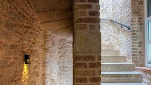 A stone staircase with a metal handrail, leading to a landing with a window.