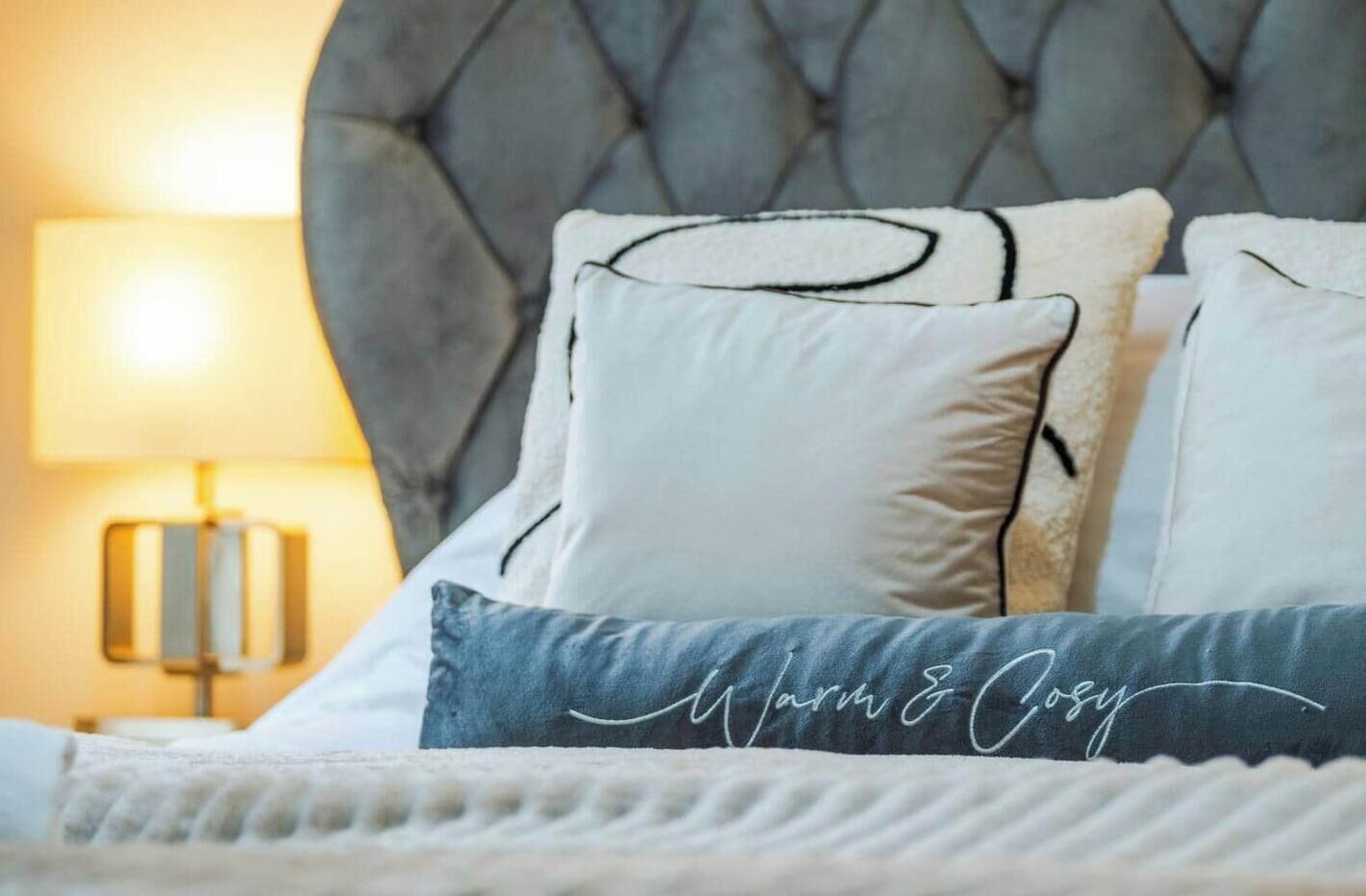 A bed with a tufted headboard, a bedside lamp, and pillows with a monogram.