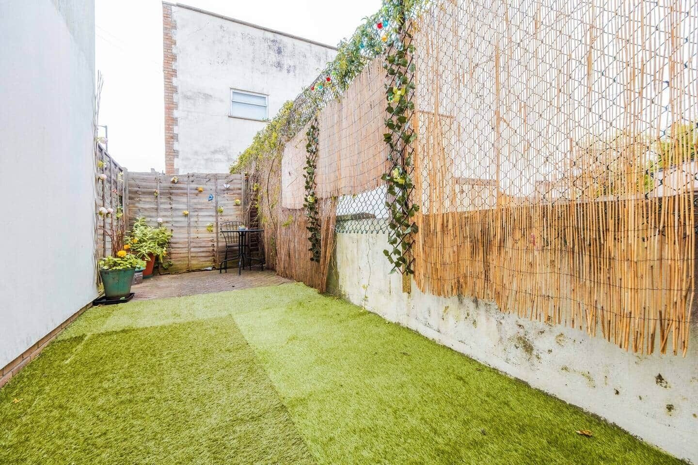 A small, enclosed outdoor space with artificial grass, a bamboo fence, and potted plants.