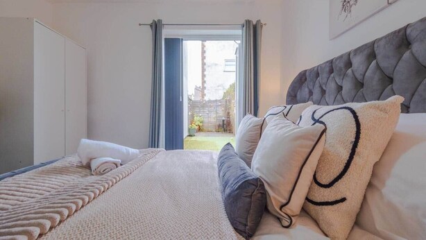 A bedroom with a bed, a grey upholstered headboard, and a view through an open door to a garden. - The Bristol Hidey-Hole (Bristol)