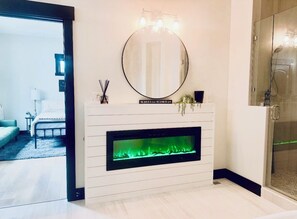 A modern bathroom with a round mirror, a built-in fireplace, and a glass shower enclosure. - LAKEFRONT Master Suite, Master Bunk Rm. Spa, Game-Rm, Bar, Pool Table, Boat Dock (Ten Mile)
