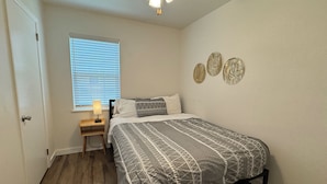 A bedroom with a bed, a nightstand, a window with blinds, a ceiling fan, and wall decor. - Tranquil 2-bedroom apartment with AC in Little Rock (Little Rock)