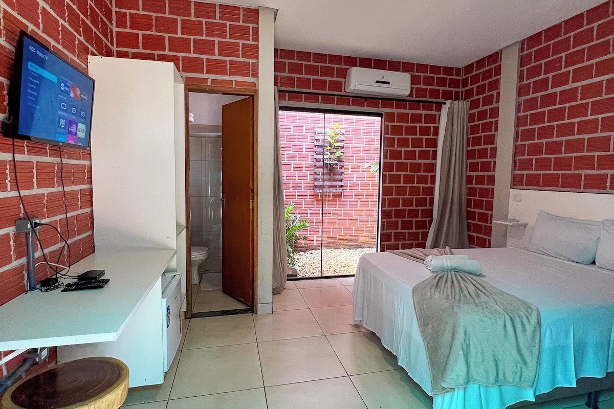 A hotel room with a TV, desk, two beds, and a view of the outside.