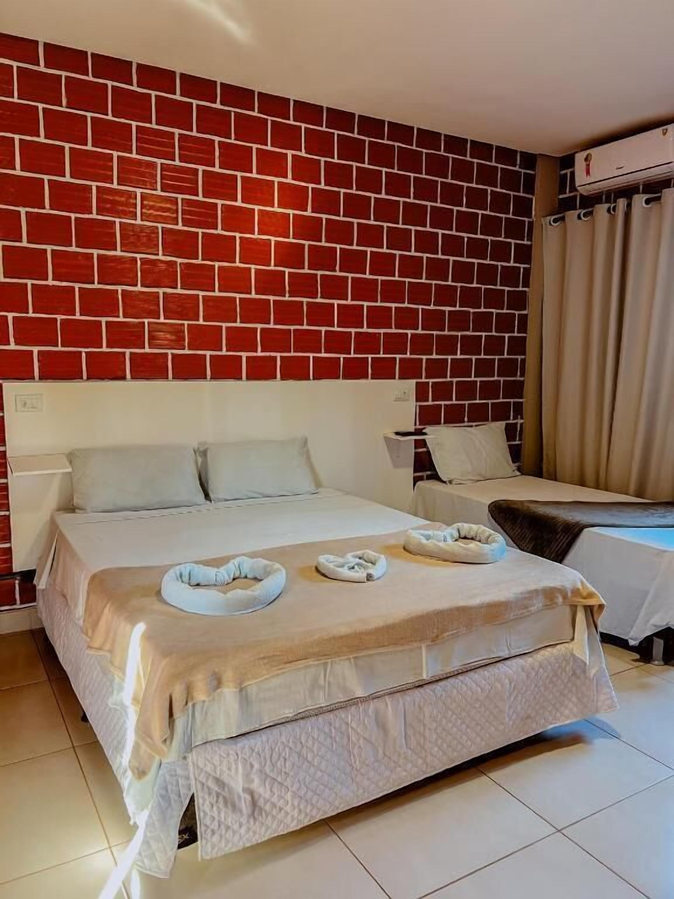 Habitación de hotel con pared de ladrillo, una cama grande con cabecera blanca, dos mesitas de noche y un escritorio pequeño.