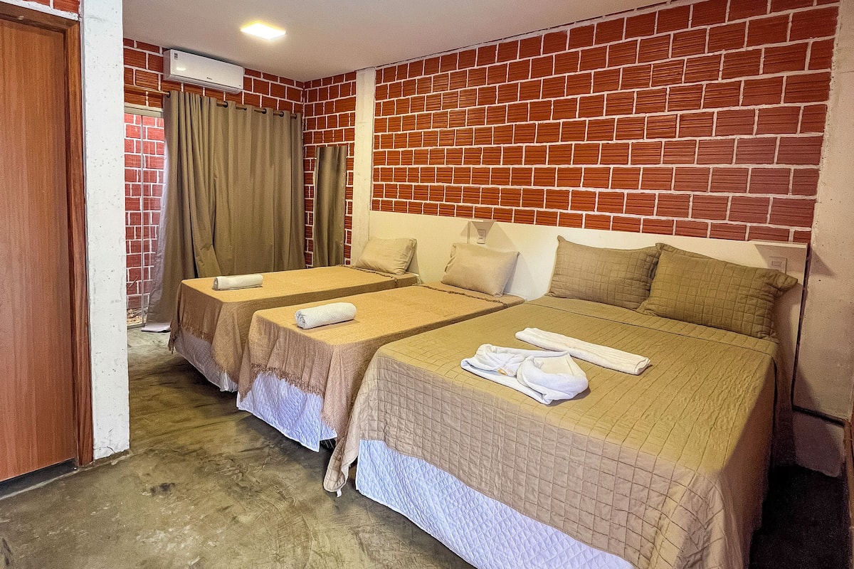 A room with two beds, a brick wall, an air conditioning unit, and a wooden door.