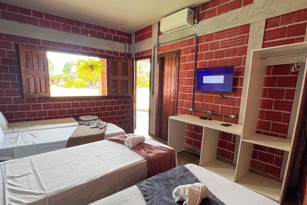 A hotel room with two beds, a TV, a window, and a brick wall.