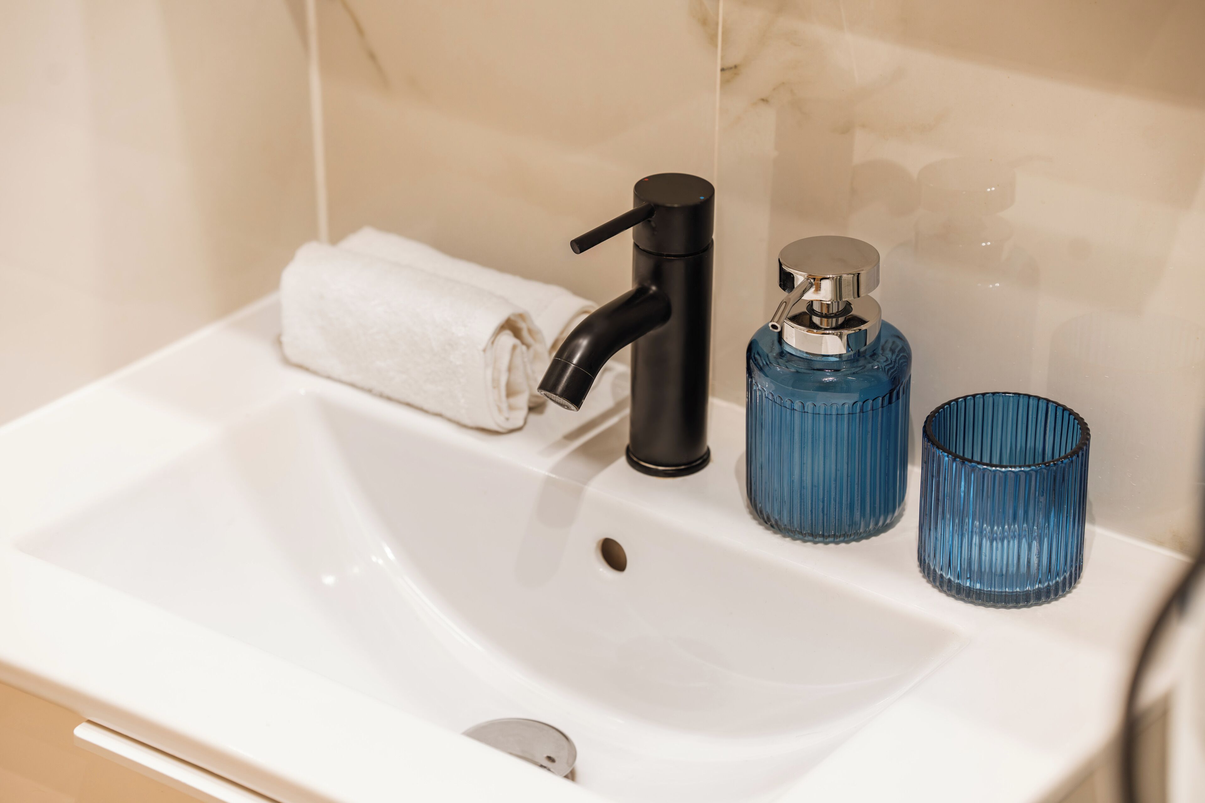 A bathroom sink with a black faucet, a blue glass bottle, and a white towel.