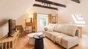A cozy loft bedroom with a sloped ceiling, a sofa, a TV, a small round table, and a window with curtains. - RentPlanet - Apartamenty Raciborska (Gliwice)