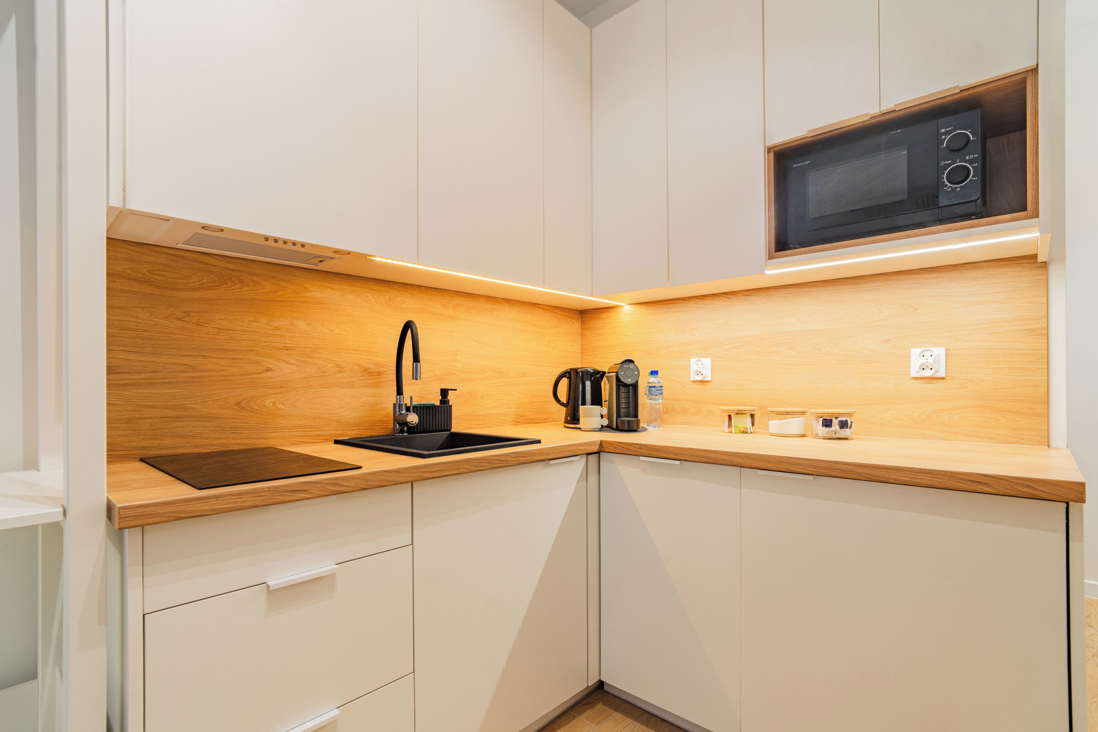A compact kitchen with a microwave, sink, and wooden countertop.