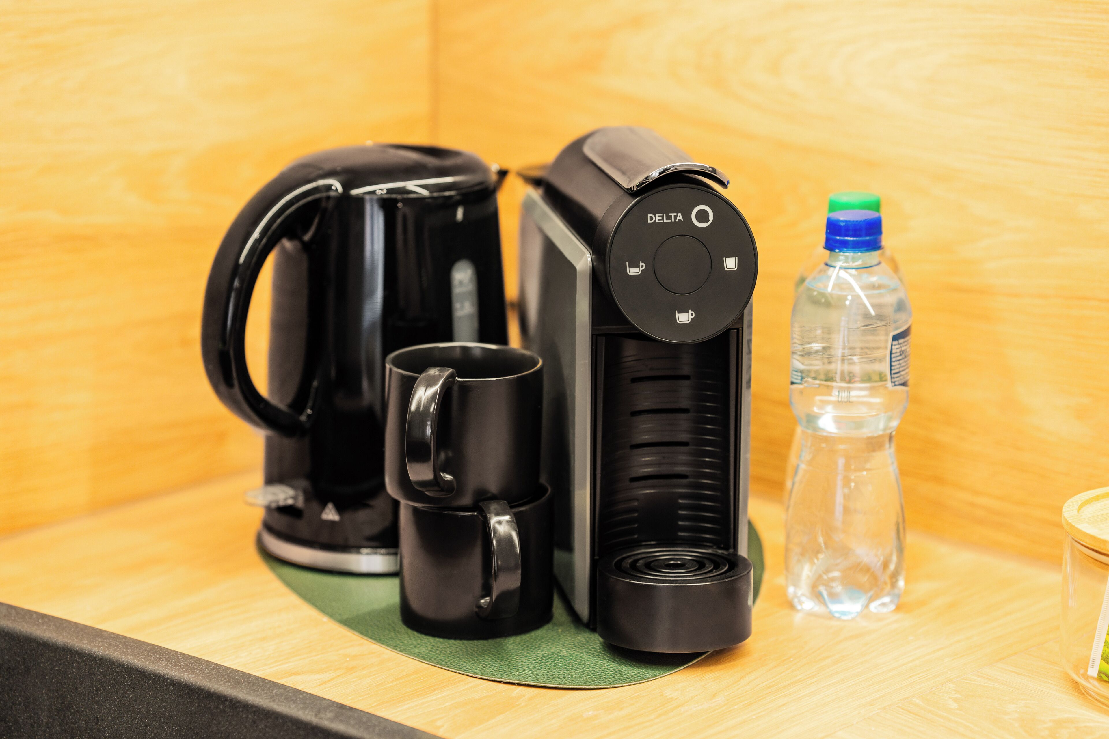A coffee maker, a water bottle, and a cup on a wooden surface.