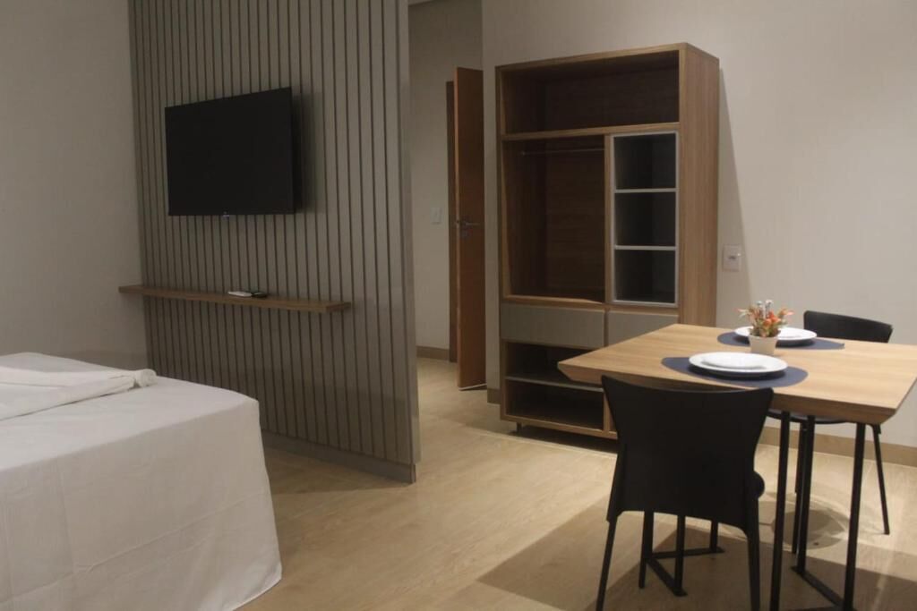 Una camera d'albergo con un letto, una TV fissata al muro, un armadio in legno e un tavolo da pranzo con sedie.