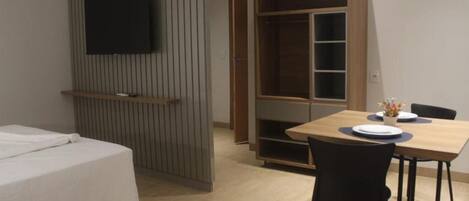 Una camera d'albergo con un letto, una TV fissata al muro, un armadio in legno e un tavolo da pranzo con sedie.